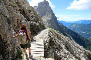 young woman crosses a wooden bridge along a stone path in the Italian Dolomites while hiking