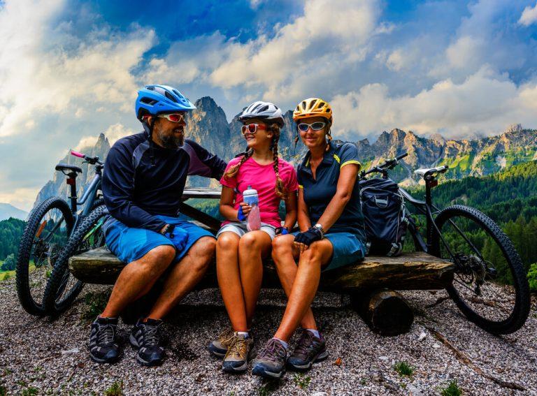 Cycling family outdoor adventure in Dolomites mountains landscape. Father, mother and daughter cycling MTB enduro trail.